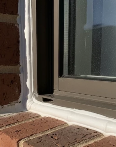 A pristine, clean line of new white waterproof caulking expertly applied around the exterior of a brick home's window in Miami